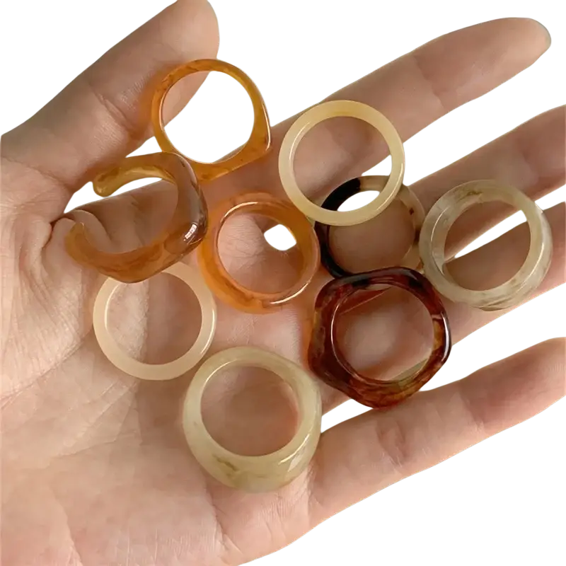 A hand holds a bohemian retro style resin stackable ring set in amber and cream translucent colors