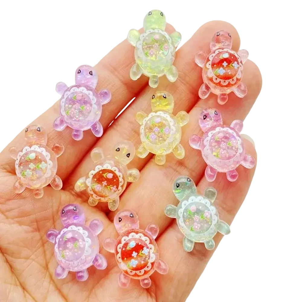 A hand holds colorful translucent resin turtle flatback charms with glittery floral interiors and lace detailing