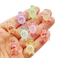 A hand holds colorful translucent resin turtle flatback charms with floral designs inside their shells 10 pack
