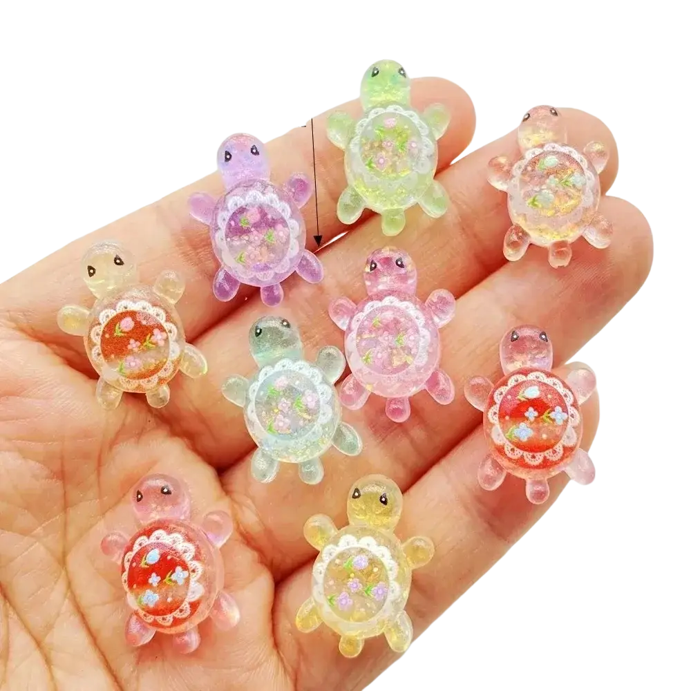 A hand holds colorful translucent resin turtle flatback charms with floral designs inside their shells 10 pack