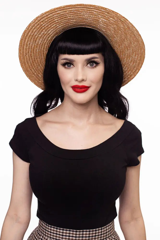 A wide-brimmed straw hat with woven texture and natural tan color paired with a black cap sleeve retro boat neck top