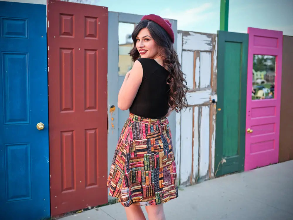 A woman wearing a black cap sleeve retro boat neck top paired with a colorful bookshelf-patterned skirt