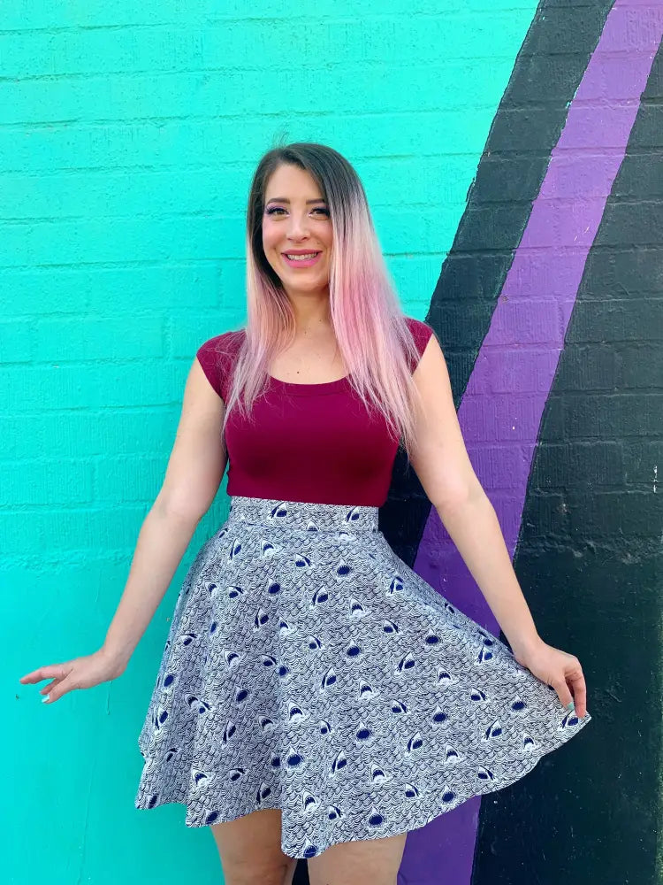A woman wears a retro burgundy boat neck cap sleeve sleeveless top with a black and white peacock feather flared skirt