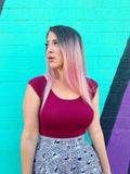 A woman wearing a retro burgundy boat neck cap sleeve fitted top paired with a patterned skirt featuring peacock feathers