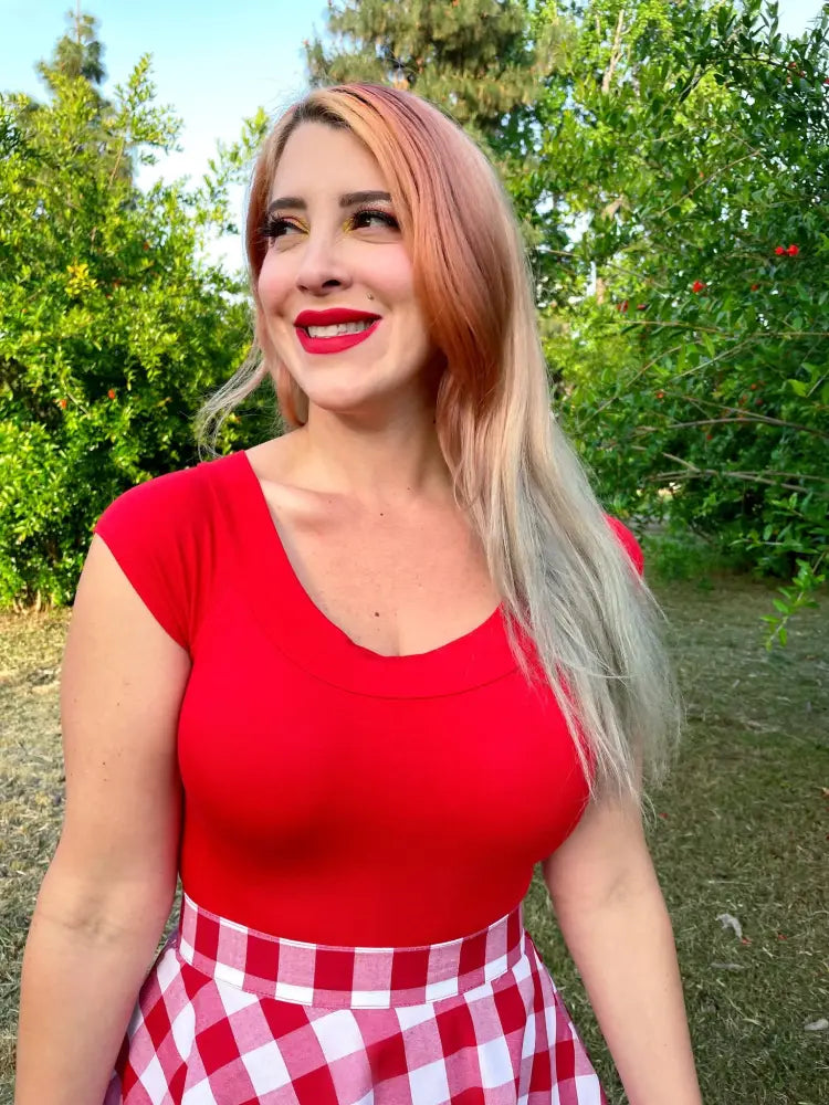 A woman wears a vintage red boat neck cap sleeve top in vibrant red paired with a red and white gingham skirt
