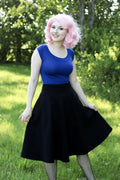 A woman wearing a royal blue retro boat neck cap sleeve sleeveless top paired with a black a-line skirt