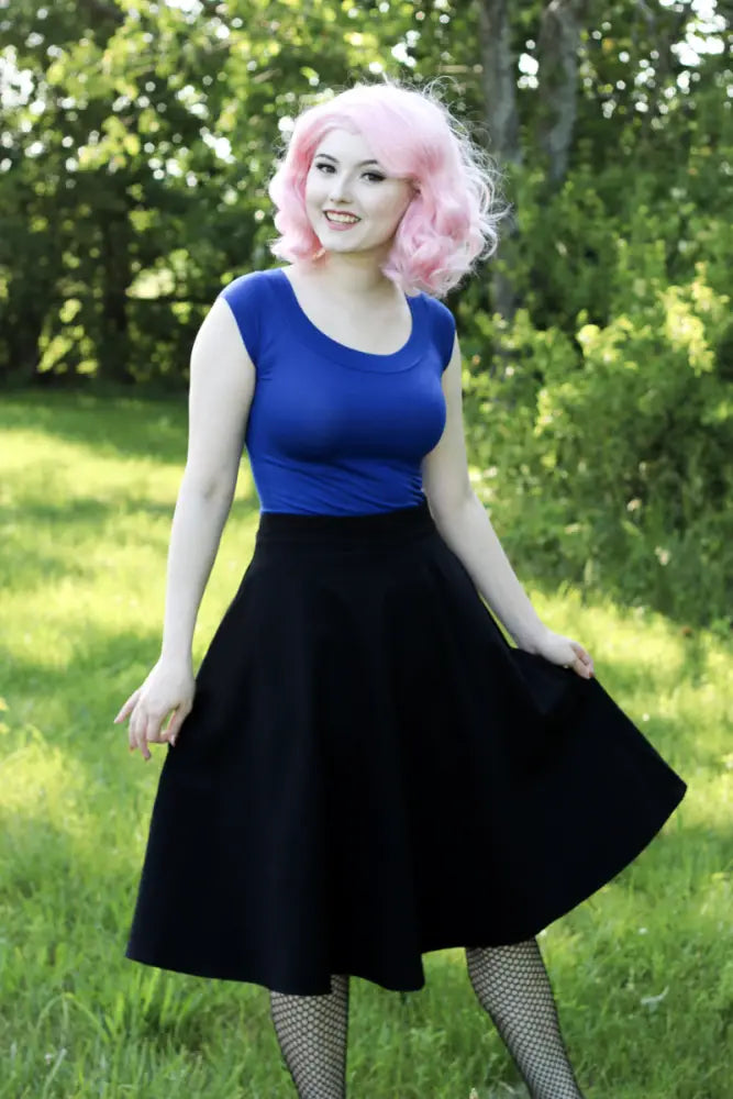 A woman wearing a royal blue retro boat neck cap sleeve sleeveless top paired with a black a-line skirt