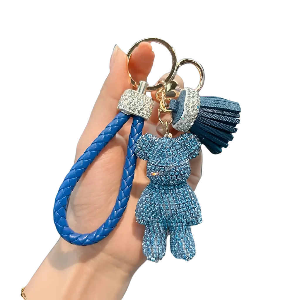 A blue braided leather keychain with a rhinestone-adorned teddy bear charm and matching tassel