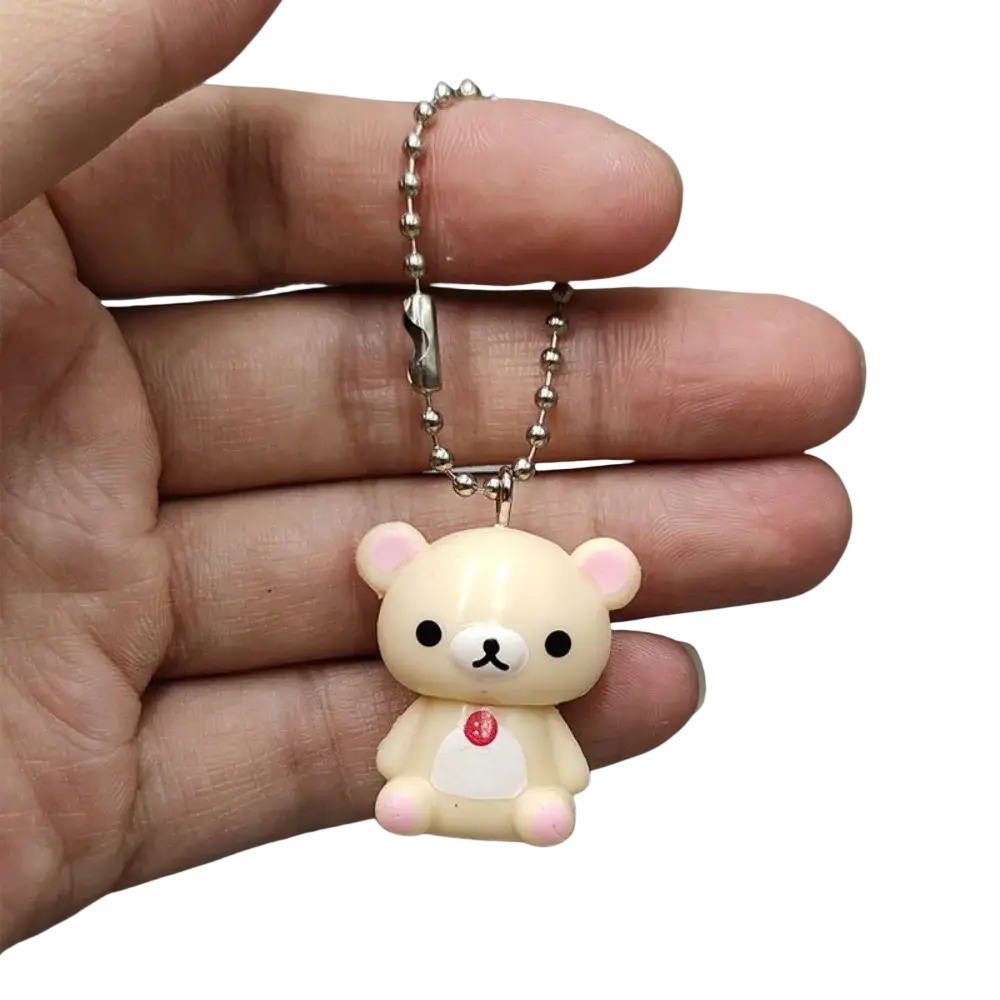 Cream-colored rilakkuma bear keychain with pink accents and red detail on white belly attached to silver ball chain