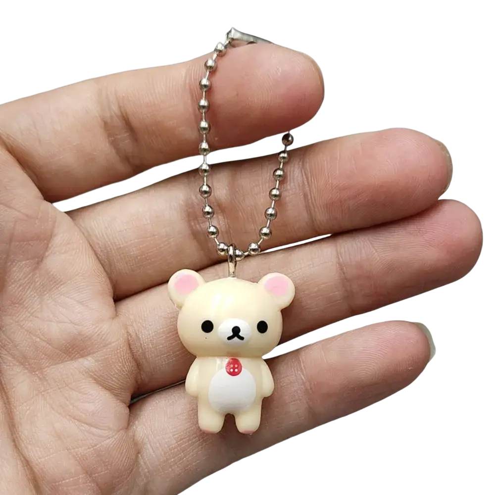 Cute cream-colored rilakkuma bear keychain with pink inner ears and red button hanging from silver ball chain pendant