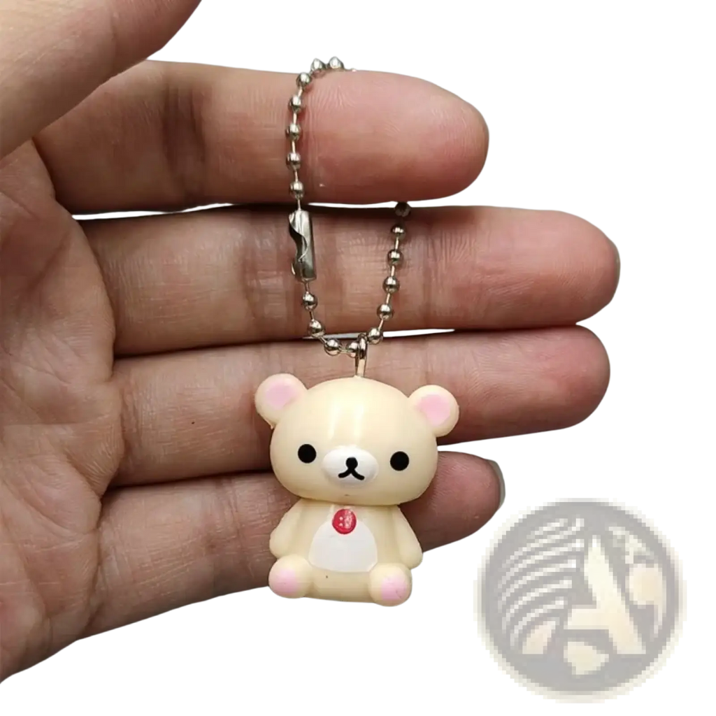 Cream-colored rilakkuma bear keychain with pink ears paws and red heart pendant attached to a silver ball chain