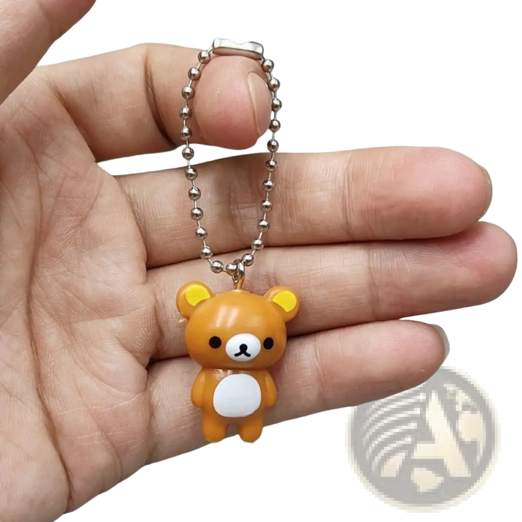 A small orange rilakkuma bear keychain with yellow ears and white belly attached to silver ball chain pendant