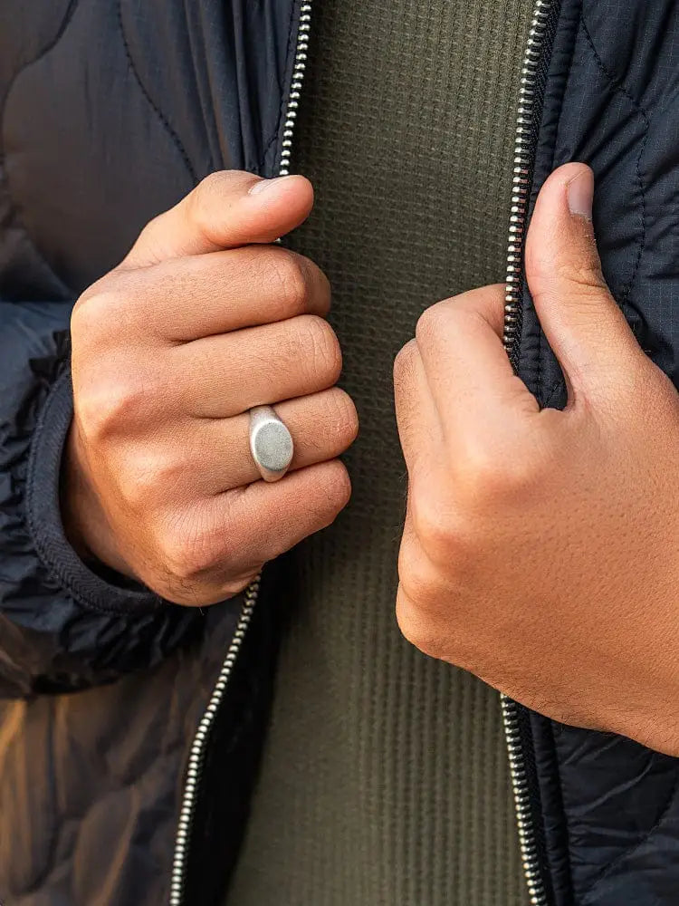 Silver oxidized round signet ring with a smooth oval face in 316l stainless steel worn on the left hand