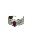 A silver band ruby halo ring with an oval-cut central ruby and diamond pavé detailing on the sides