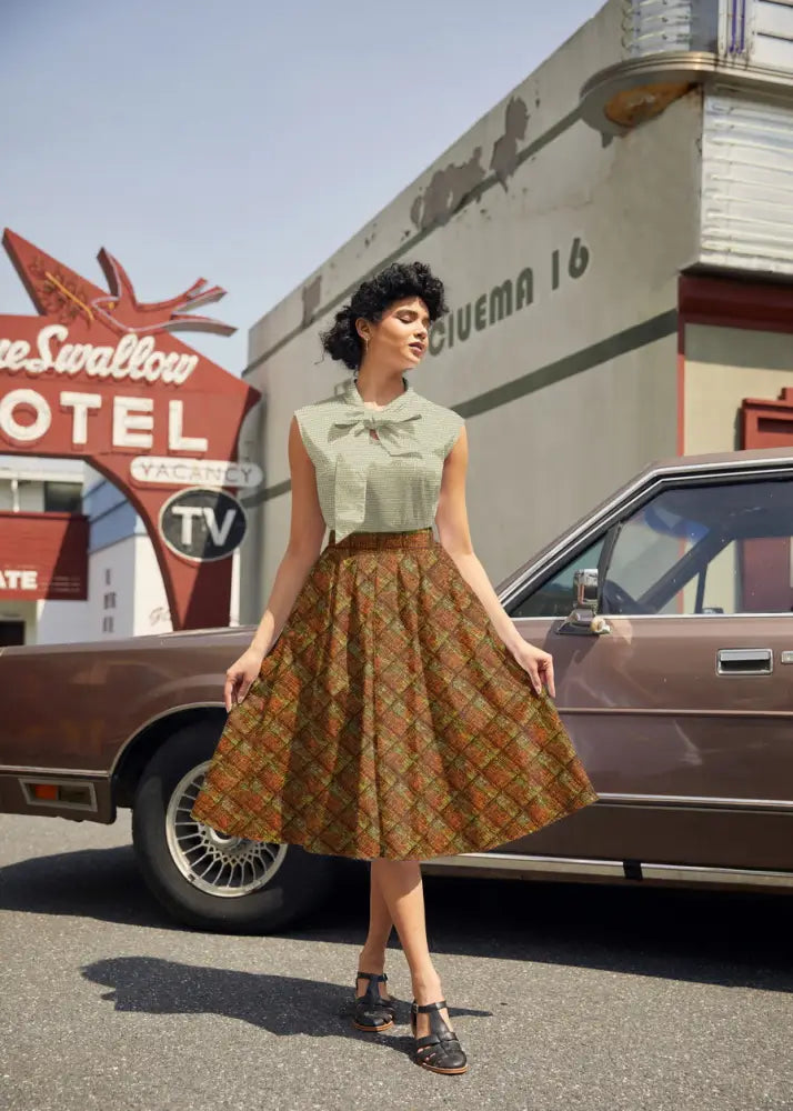 A woman wears a rust plaid Doris retro A-line cotton skirt with pockets paired with a light green sleeveless top