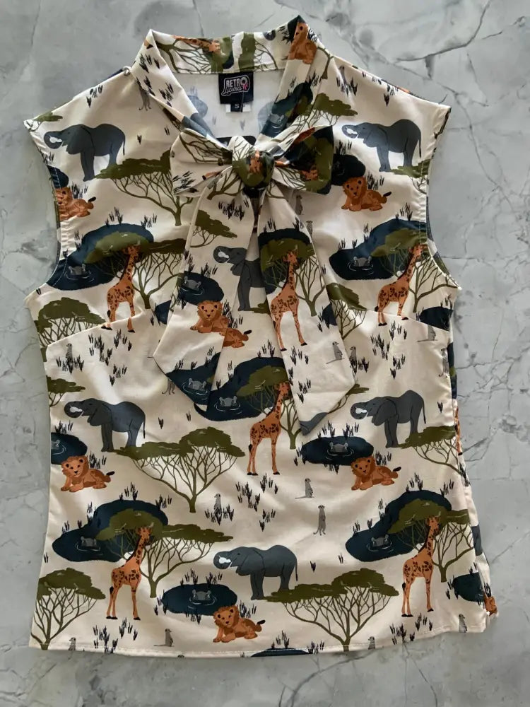 Sleeveless cream-colored cotton blouse with safari animal print and bow neck featuring elephants giraffes and lions