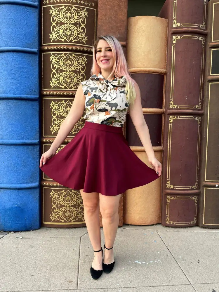A woman wearing a sleeveless safari animal print cotton blouse with bow neckline paired with a flared maroon skirt