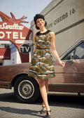 A woman wearing a sleeveless olive green cotton safari print retro dress with peter pan collar and black belt