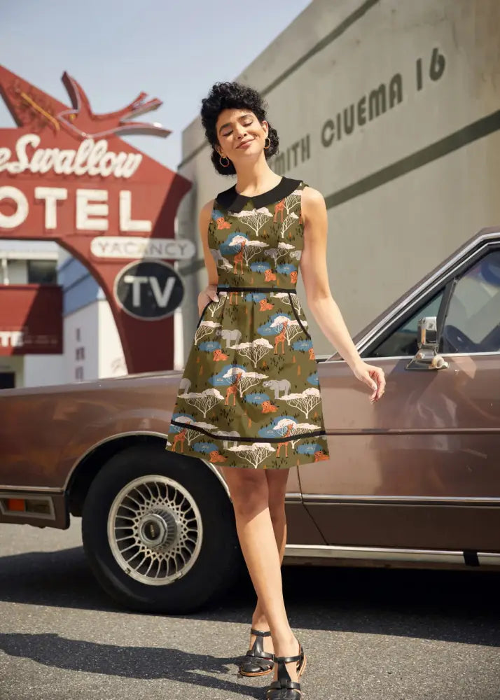 A woman wearing a sleeveless olive green cotton safari print retro dress with peter pan collar and black belt