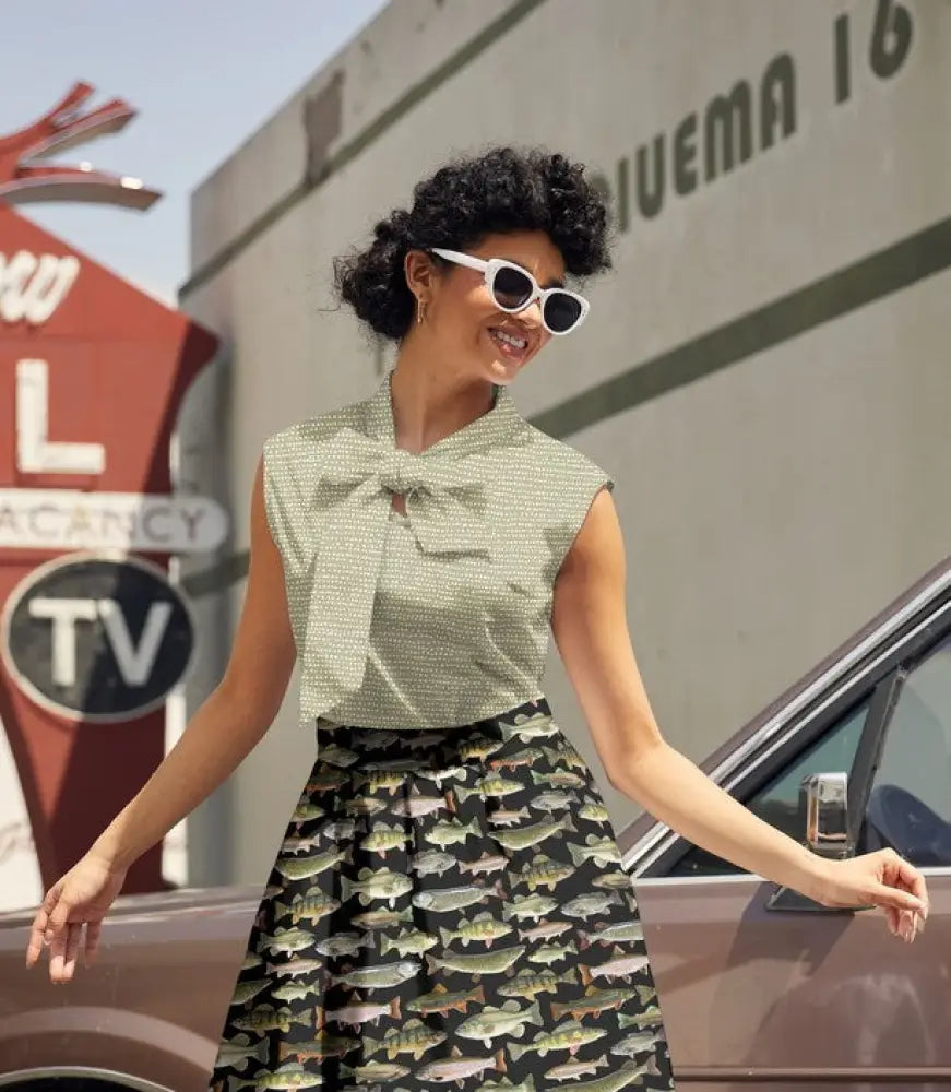 A woman wears a sleeveless sage dot bow neck vintage cotton blouse with a light green patterned design