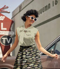 A woman wears a sleeveless sage dot bow neck vintage cotton blouse with a light green patterned design