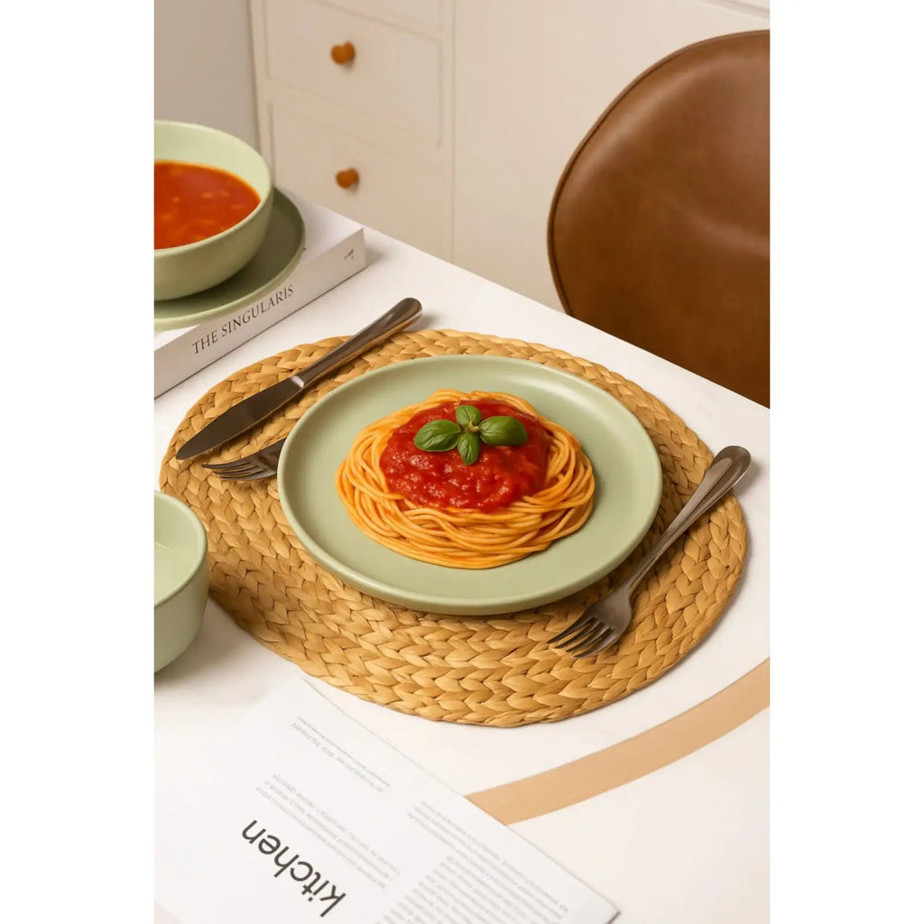 A light green ceramic plate from the sage green 12 piece stoneware dinnerware set holding spaghetti with tomato sauce and basil