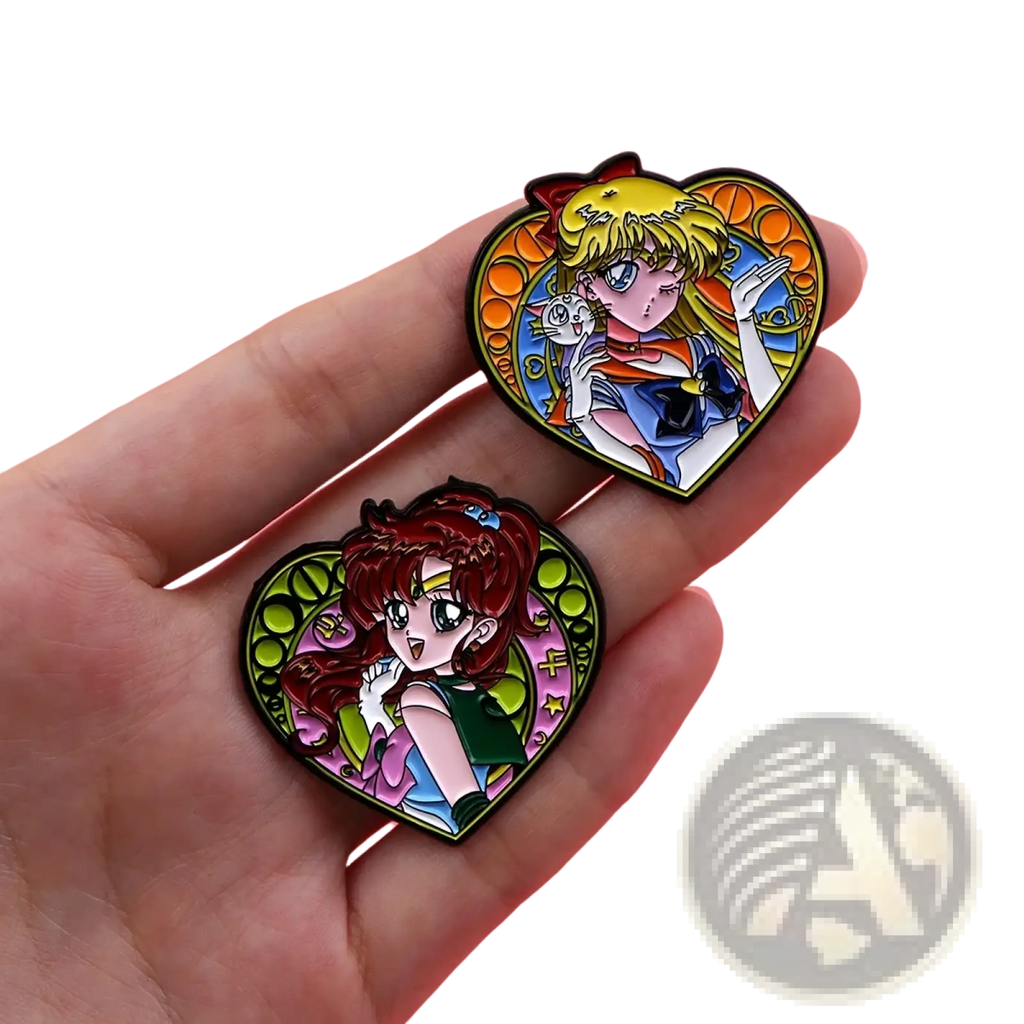 Two heart-shaped enamel pins featuring blonde and red-haired anime characters from sailor moon on pink background