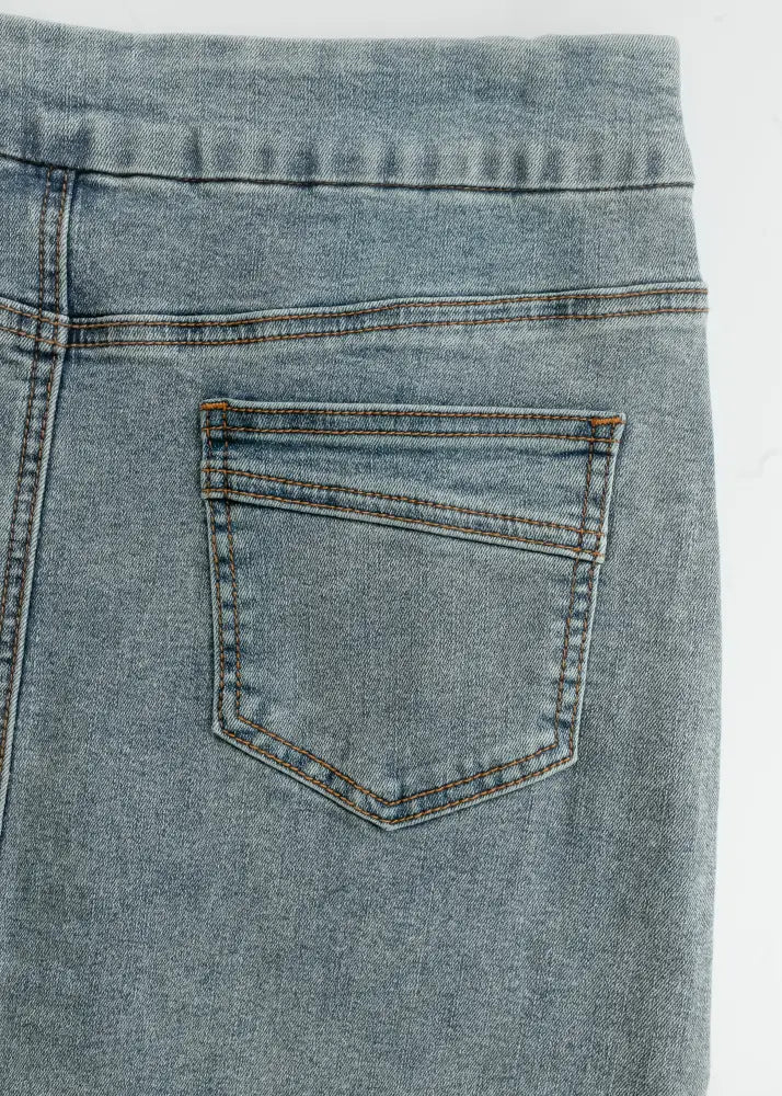 Back side of sandra classic light wash straight denim midi skirt featuring a classic pocket with brown stitching
