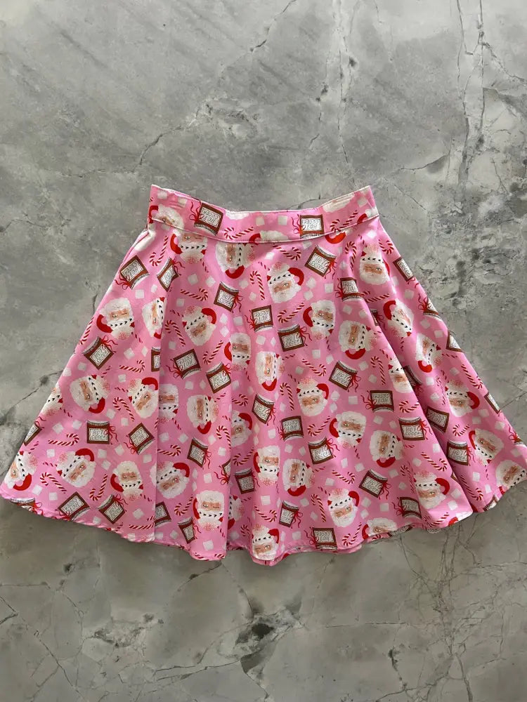 Pink pleated Christmas skater skirt with festive Santa Claus faces candy canes and chocolate bars pattern