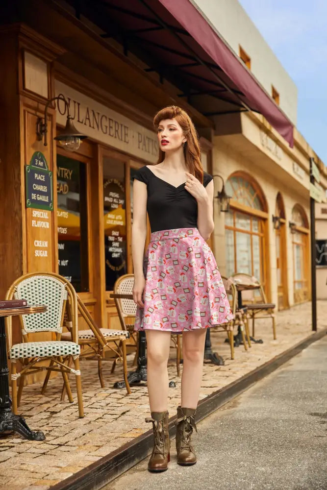 Woman wearing a pink pleated Christmas skater skirt with playful pastel geometric patterns in front of a bakery