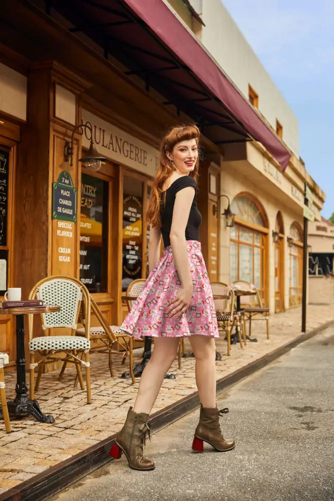 A woman wearing a Santa mugs pink pleated Christmas skater skirt with red hearts and brown heeled boots with red block heels