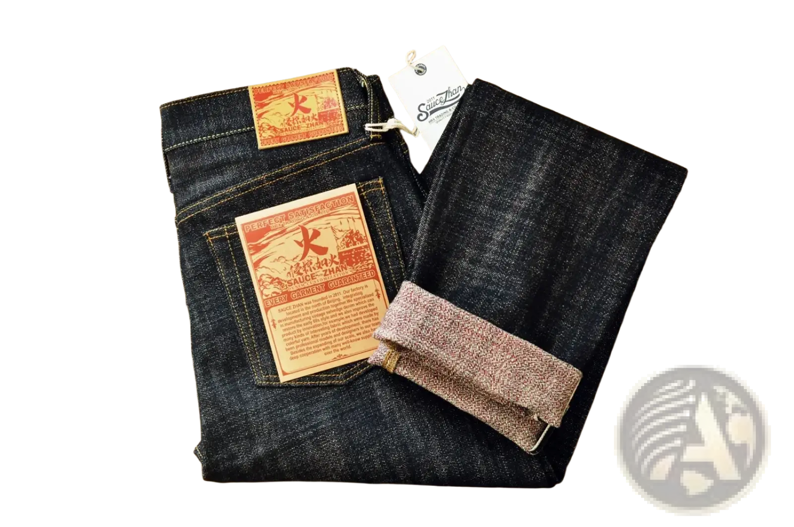 Dark indigo Saucezhan Fire Selvedge tapered raw denim jeans with red and orange branded patches folded on wood surface