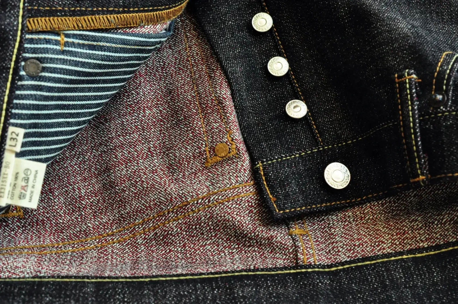 Saucezhan Fire Selvedge tapered raw denim jeans in dark indigo with tan stitching silver buttons and striped lining
