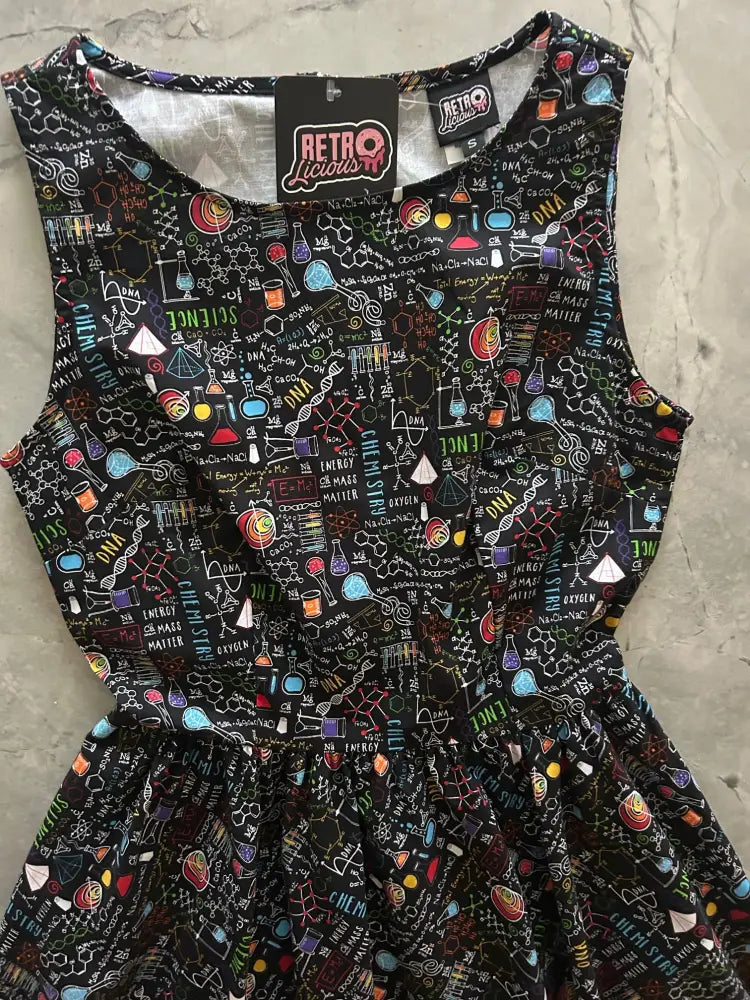 Black sleeveless 1950s cotton midi dress with pockets featuring vibrant colorful science print and lab equipment design