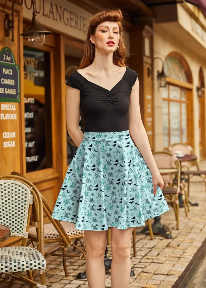 A light blue cotton sea skater a-line skirt with nautical print of black birds and green cactus plants worn with black top