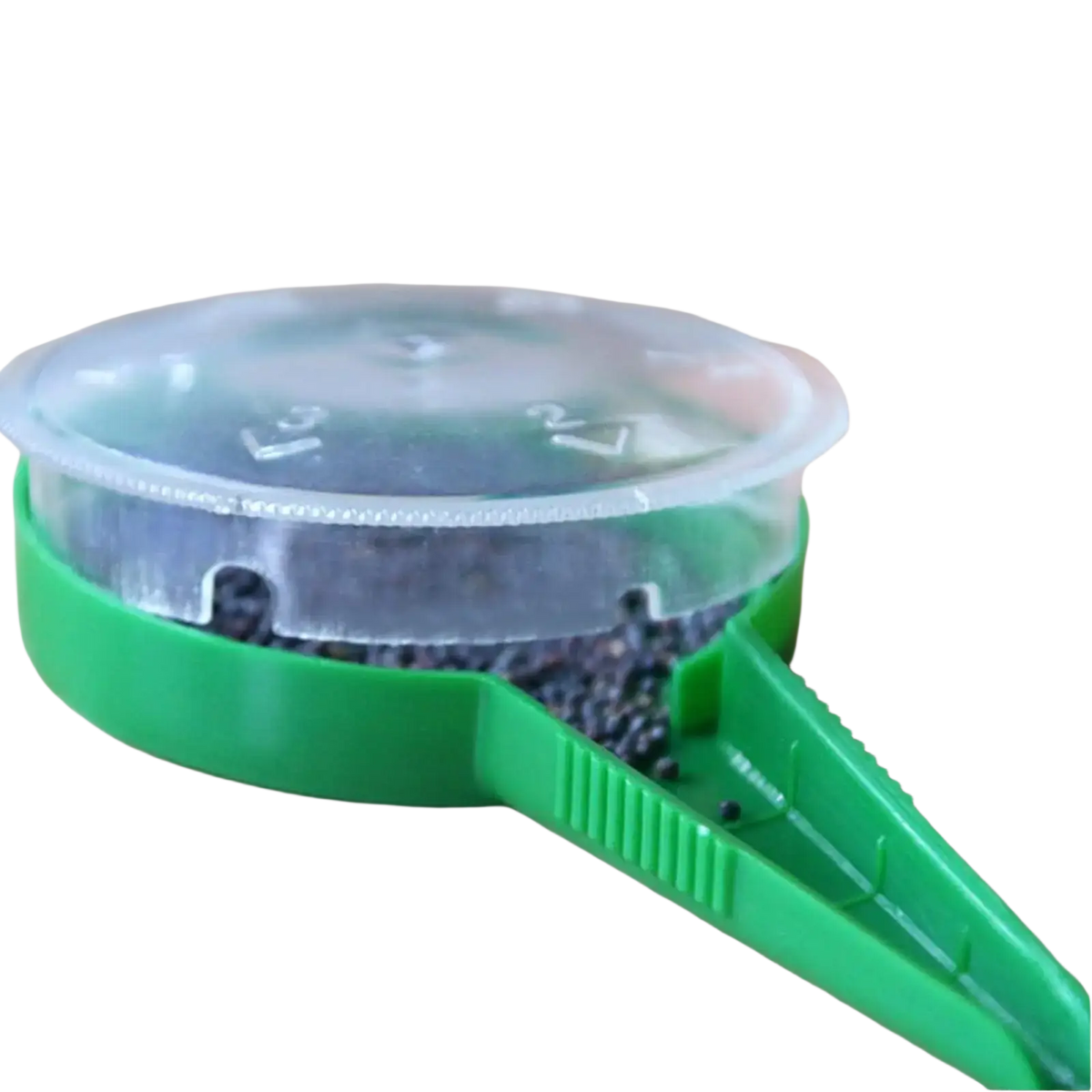 Green plastic handheld seed sower with clear lid containing small black seeds for precise planting tasks