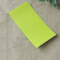 A sleek lime-green rectangular sticky note pad with a smooth matte finish shown alongside navy blue leather sofa repair patch