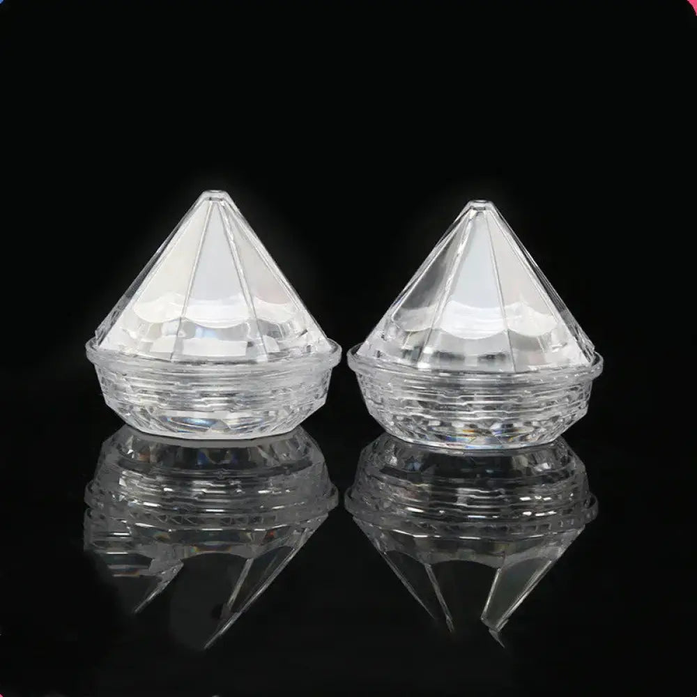 Two clear faceted diamond-shaped acrylic refillable travel cosmetic bottles with textured bases