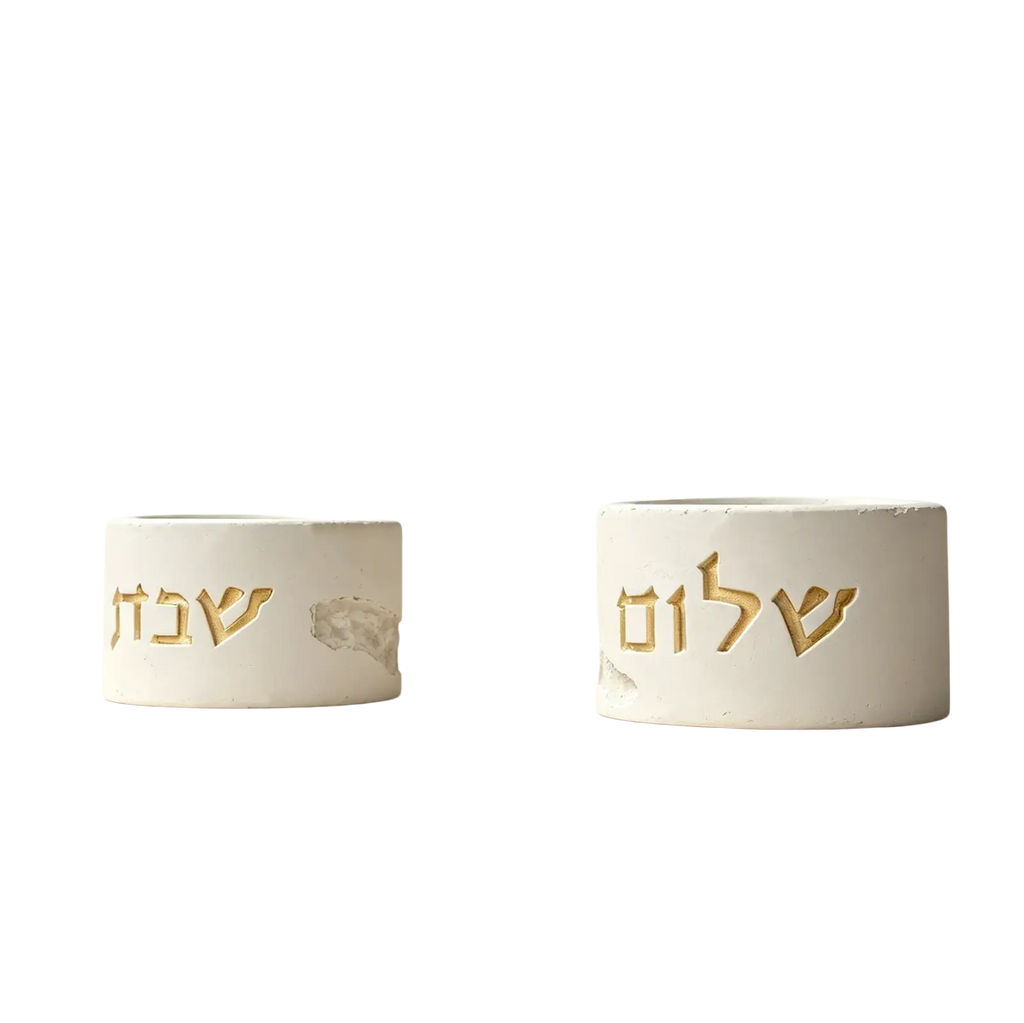 Two white concrete shabbat candle holders with gold hebrew lettering made from silicone mold material