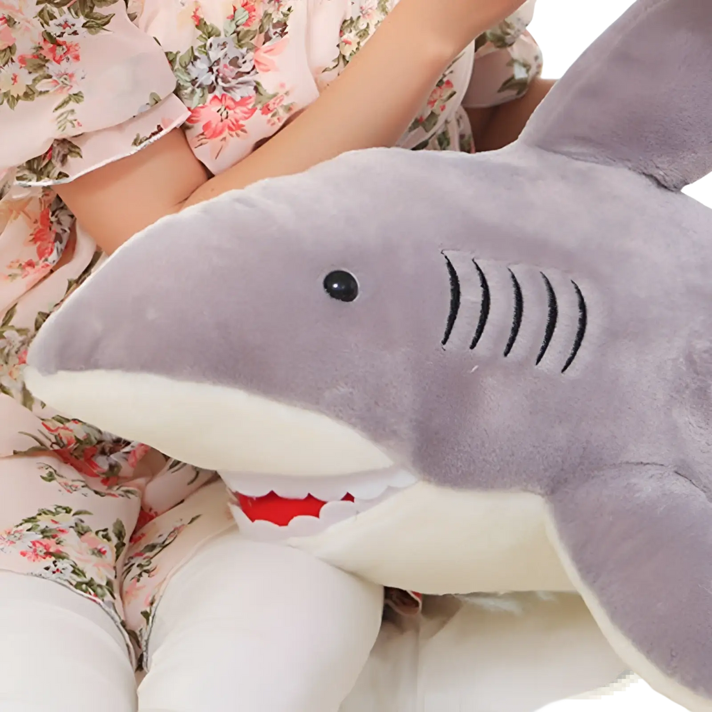 Shark plush toy with gray fabric, white underbelly, red stitched teeth, and black embroidered gills