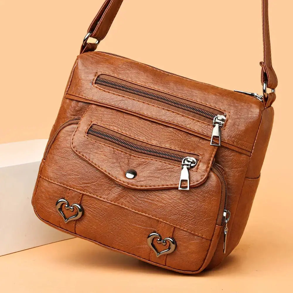 Brown leather faux leather crossbody bag with silver heart-shaped studs and multiple zippers for women