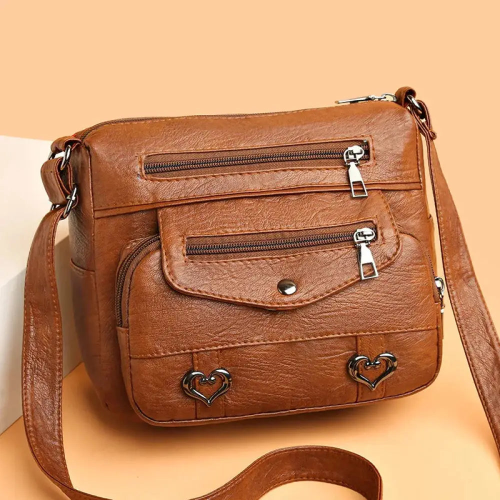 Brown faux leather women’s crossbody bag with silver heart studs and multiple zippers for organized storage