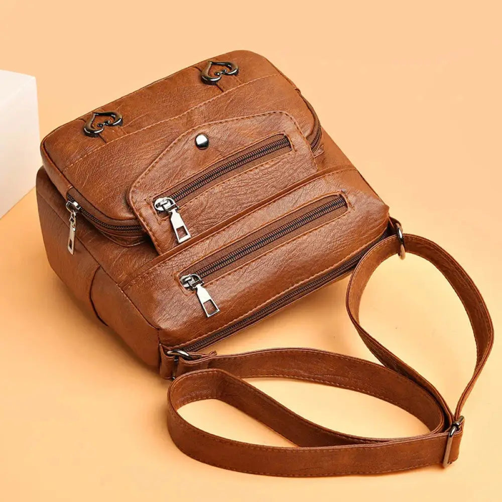 Brown faux leather crossbody bag for women with multiple zippers and heart-shaped metal clasps for organization