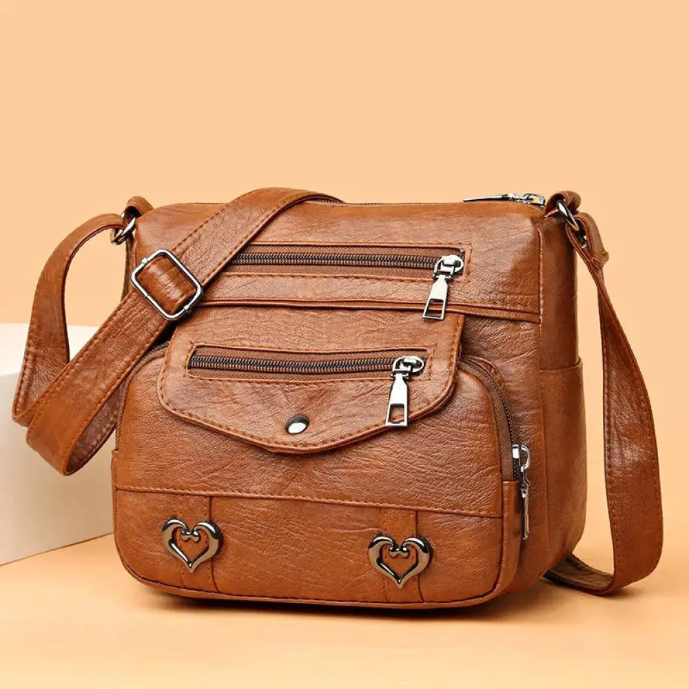 Women’s brown faux leather crossbody bag with multiple zippers and heart-shaped metal studs for organized use