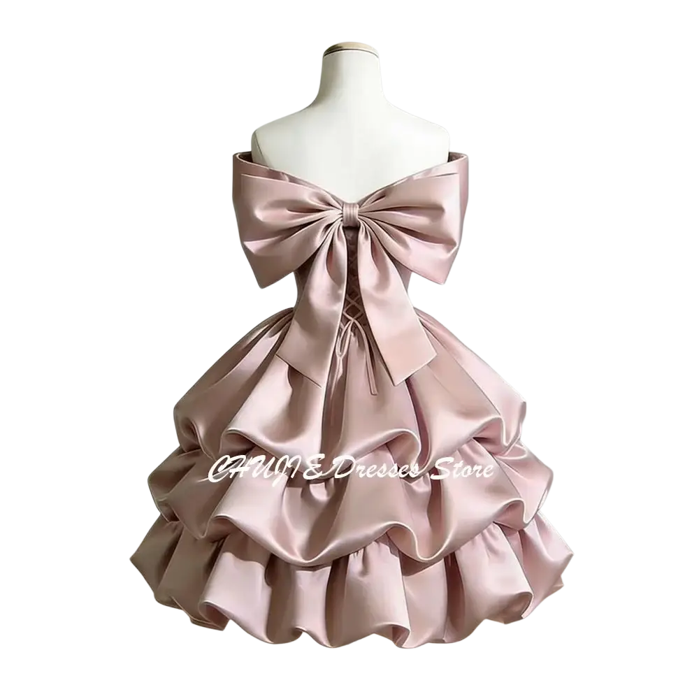 A blush pink satin off-shoulder tiered graduation dress showing the back with a large bow and ruffles