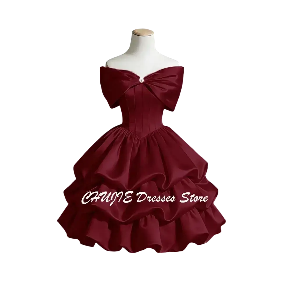 A deep burgundy satin graduation dress featuring an off-shoulder design with a large bow and layered ruffles