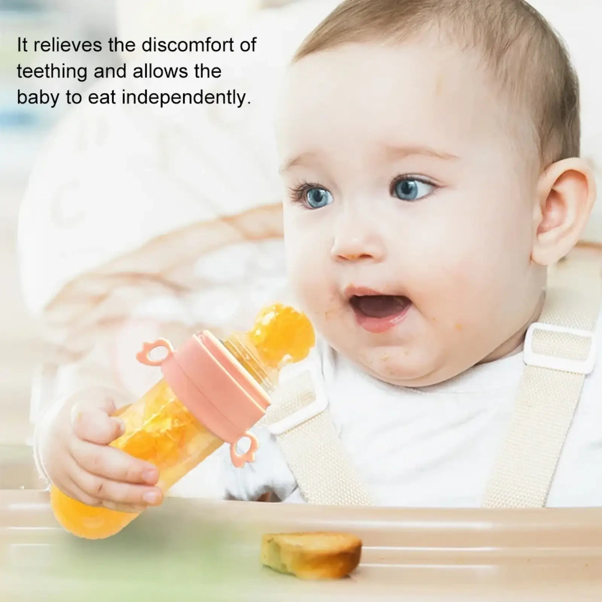 Pink silicone baby squeeze feeding bottle with orange fruit pieces inside designed for teething and spoon feeding