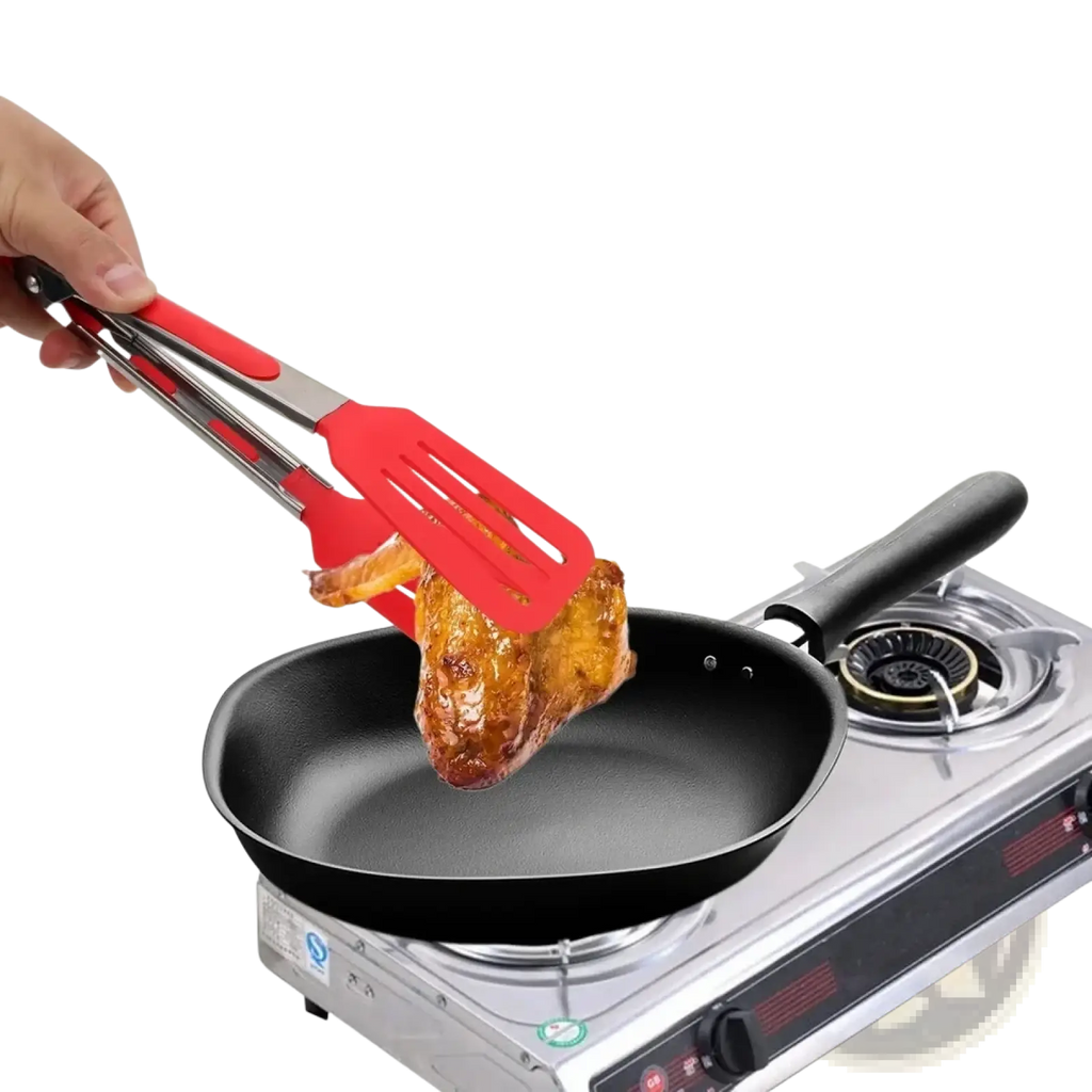 Red silicone kitchen tongs with stainless steel handles lifting roasted chicken from a black non-stick frying pan