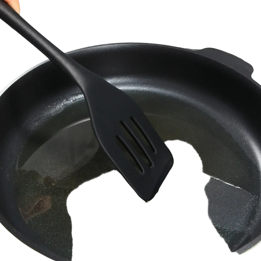 Black silicone kitchen turner spatula with long handle and three slits resting in a frying pan for cooking tasks