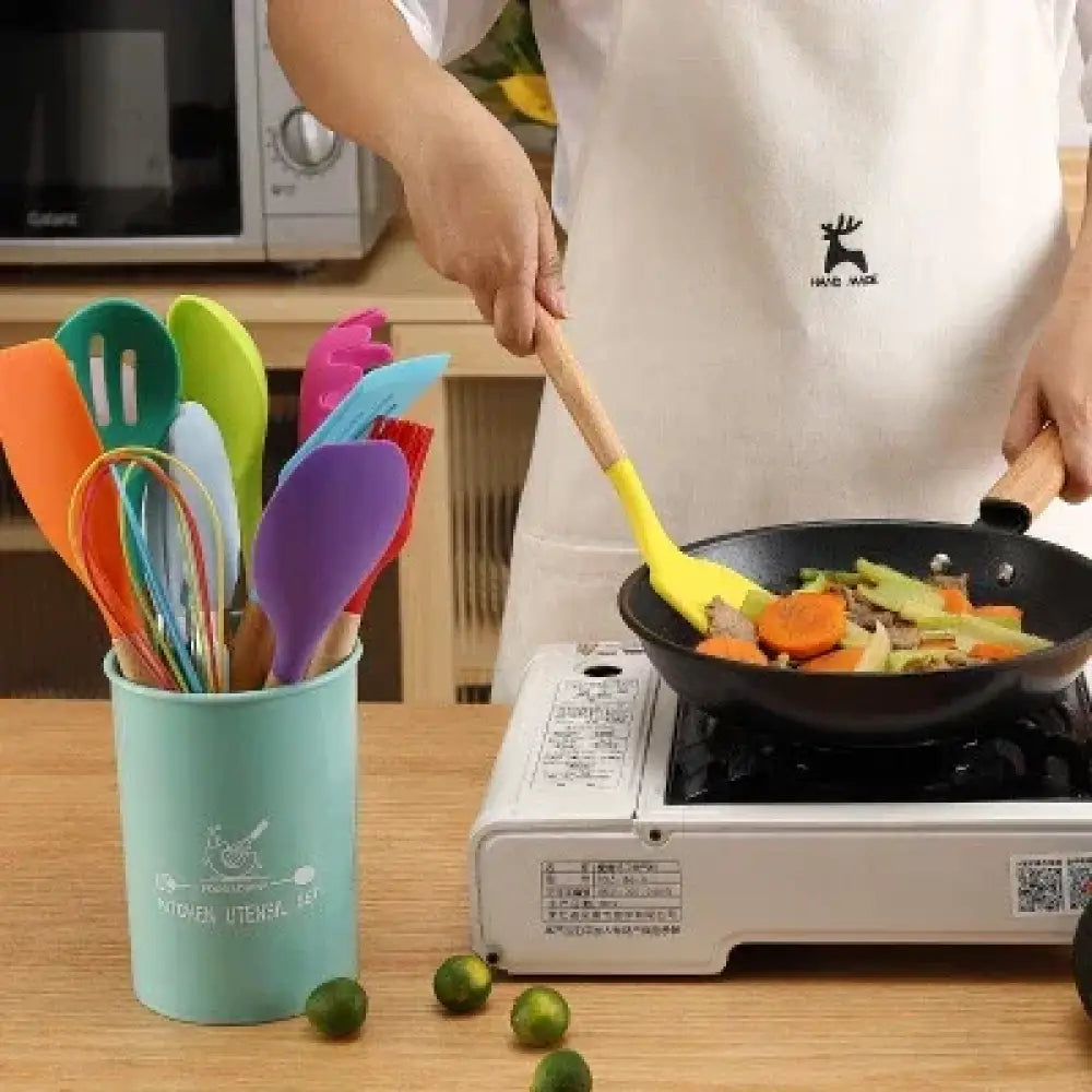 A vibrant yellow silicone and wood heat resistant spatula stirring vegetables in a black frying pan